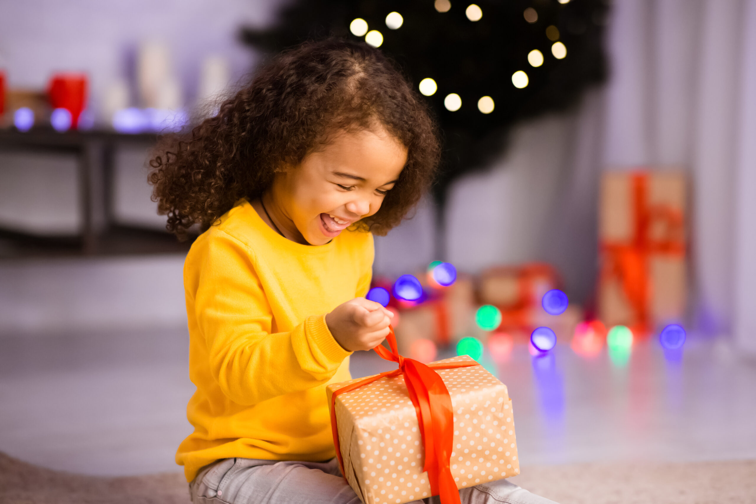 Emotional happy girl opening desired Christmas gift at home