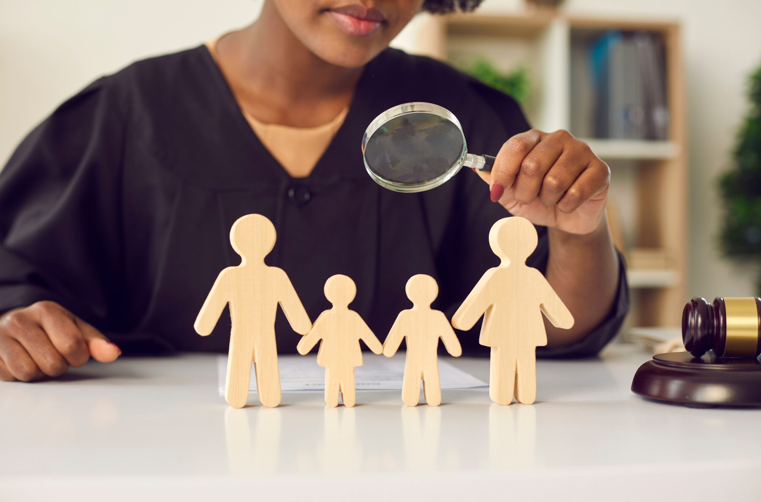 judge in black gown with magnifying glass looking on family wood figure. Cropped shot. Disputes mediation, children custody by parents after divorce court decision